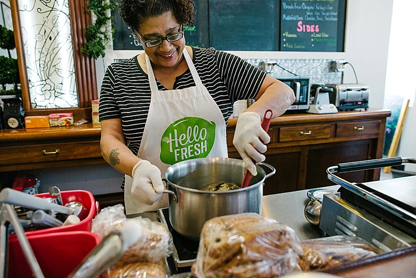 woman wearing Hello Fresh apron stirring pot of soup at cafe
