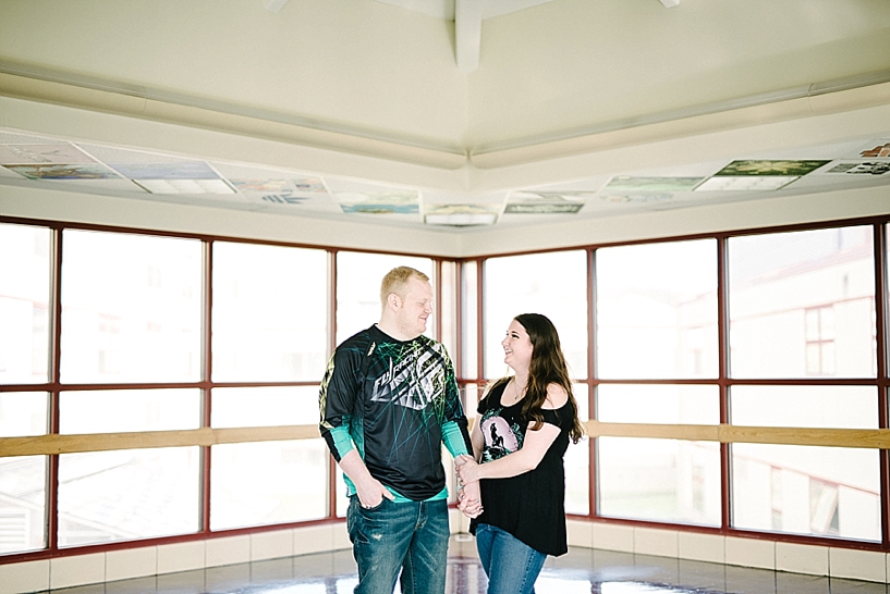 couple wearing black and teal shirts standing in front of floor to ceiling windows