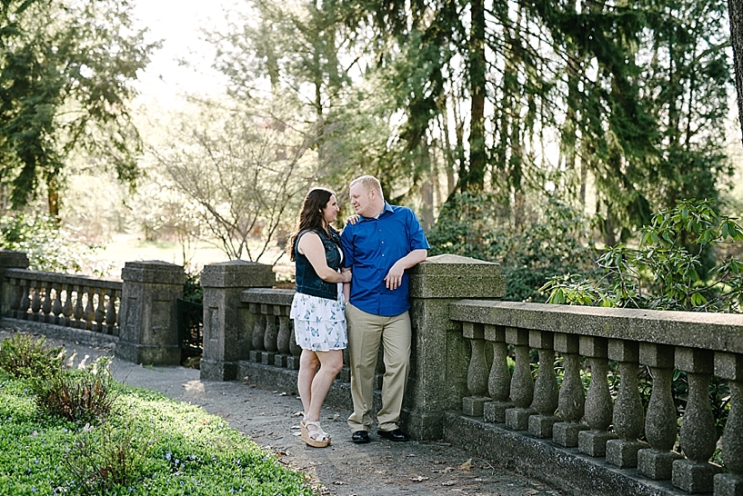 engaged couple standing by stone wall in Buhl Park Rose Garden