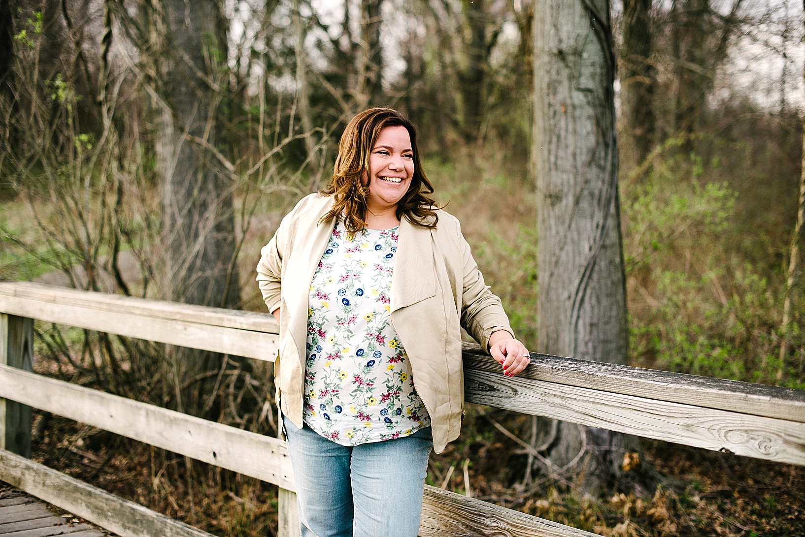 woman wearing floral print shirt, blazer, and jeans standing on wooden bridge