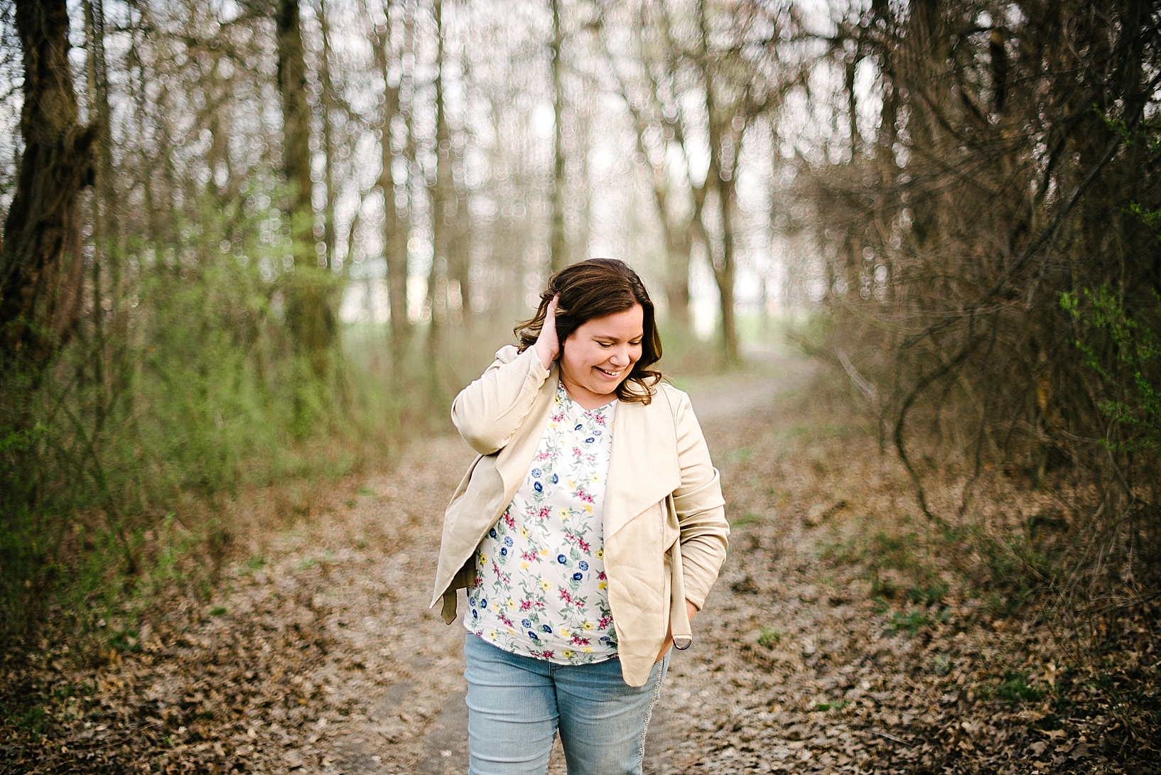 woman wearing floral print shirt, blazer, and jeans on trail in middle of woods