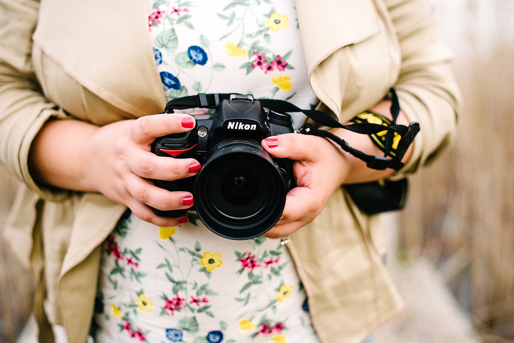 Nikon camera in woman's hands with painted red fingernails wearing floral print shirt and blazer
