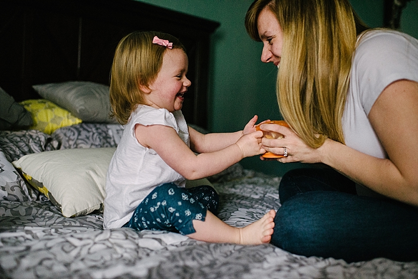 mom and daughter laughing sitting on bed playing with snack cup