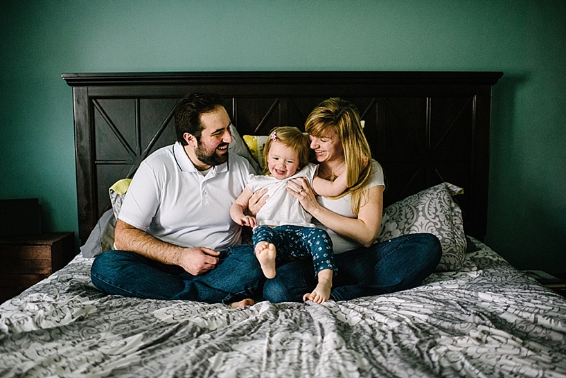 man and woman sitting on bed with toddler daughter in their lap