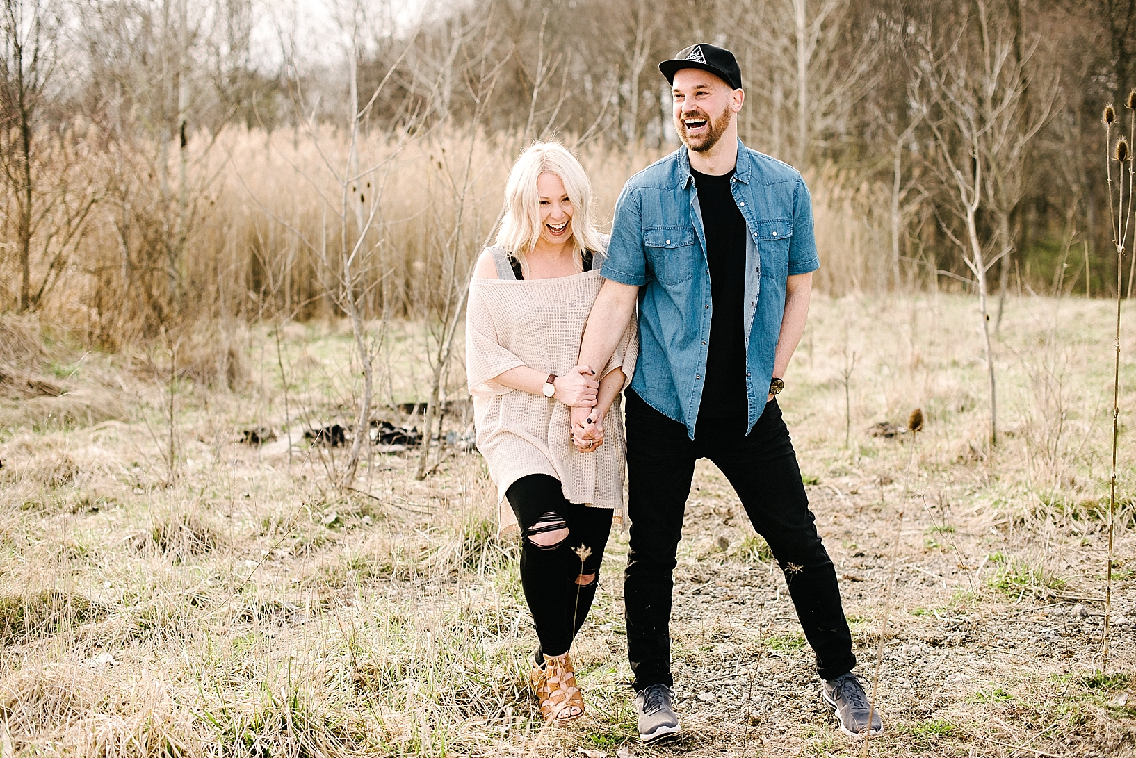 trendy hipster couple holding hands and laughing outside in field