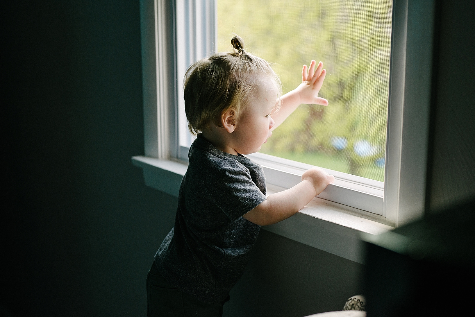 toddler boy with man bun looking out window