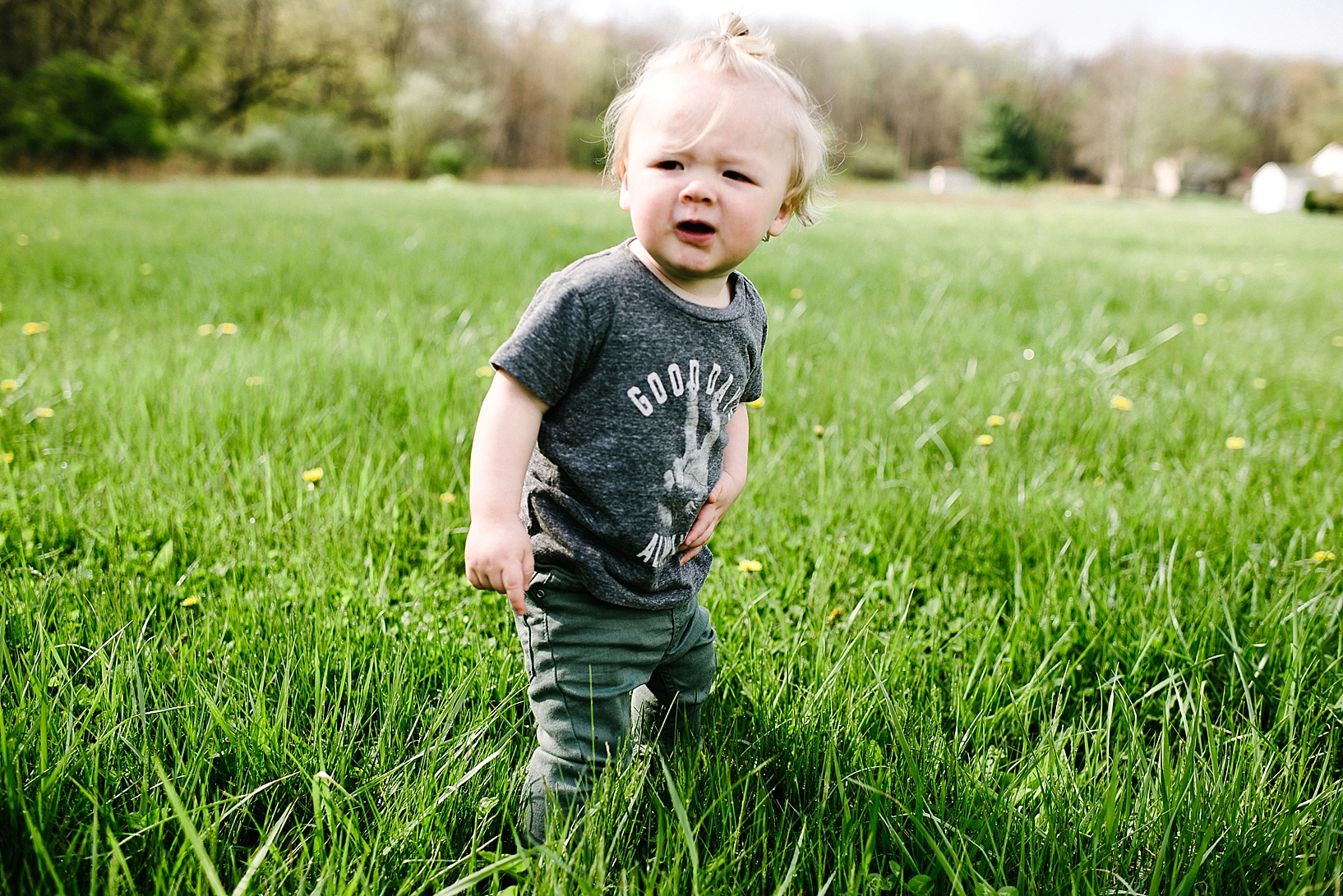 hipster baby standing in field of grass wearing man bun and Good Vibes tshirt
