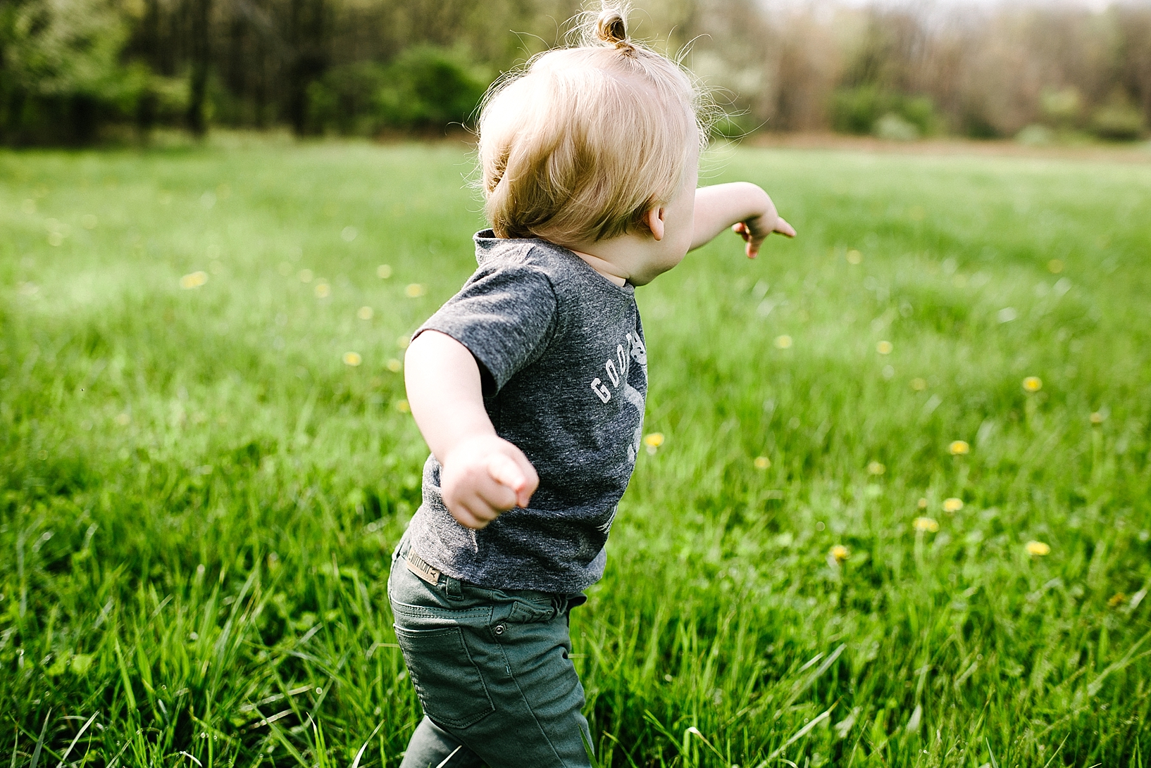 hipster baby standing in field of grass wearing man bun and pointing