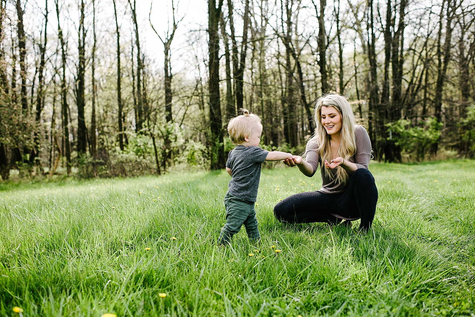 mother and toddler son in open field of grass by forest