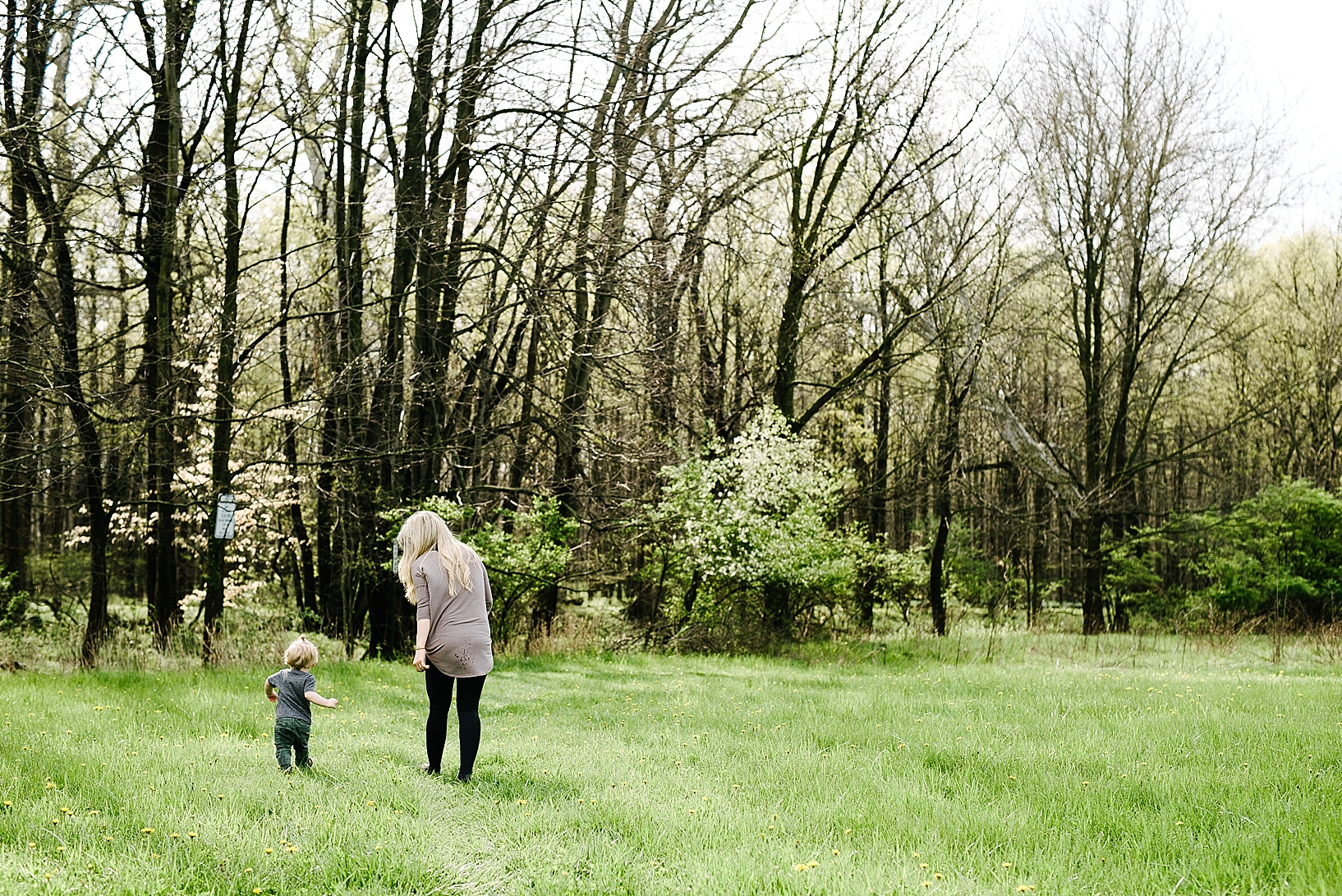 mother with long blonde hair and toddler son walking across field