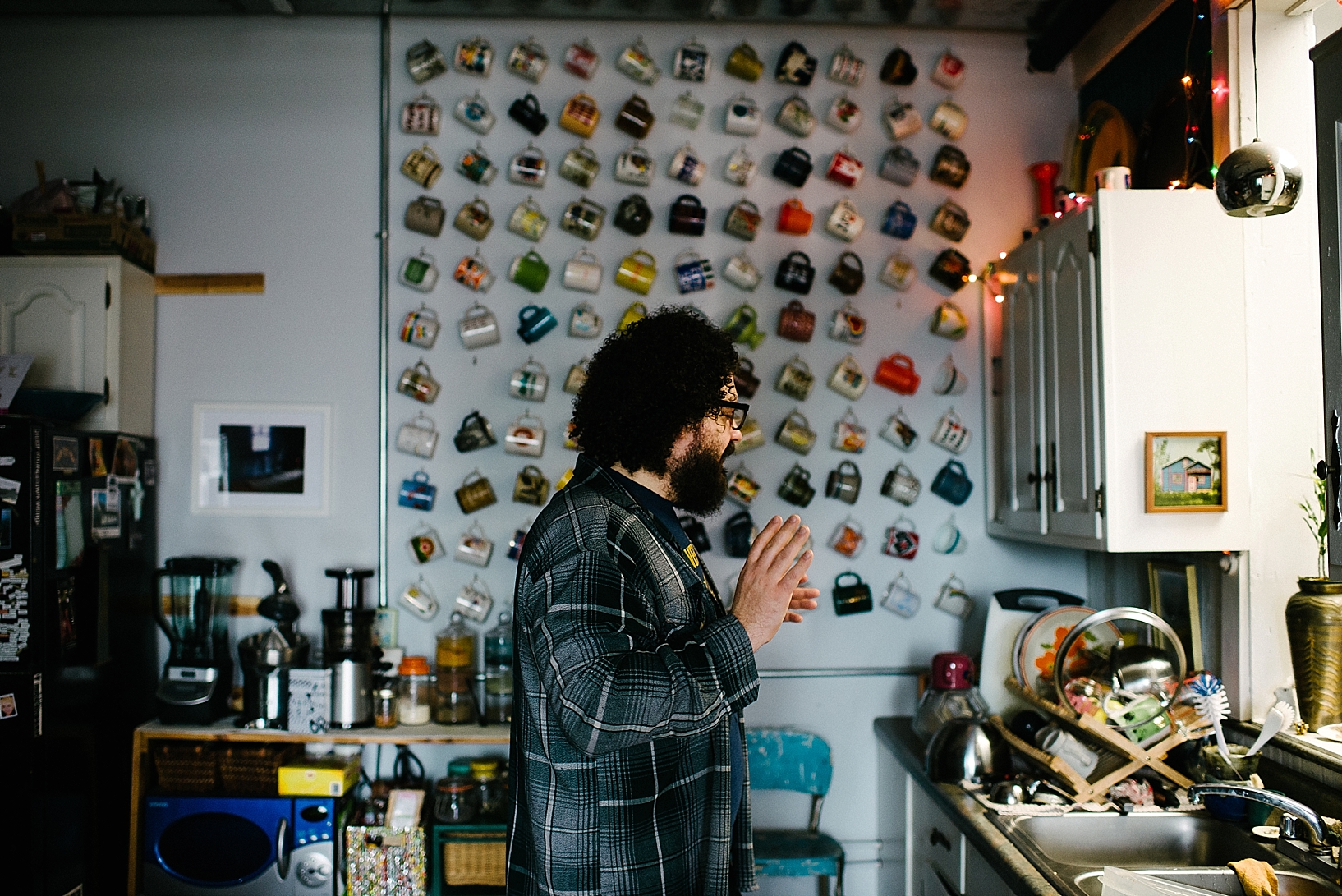 man with curly hair and beard standing in kitchen in front of mug wall
