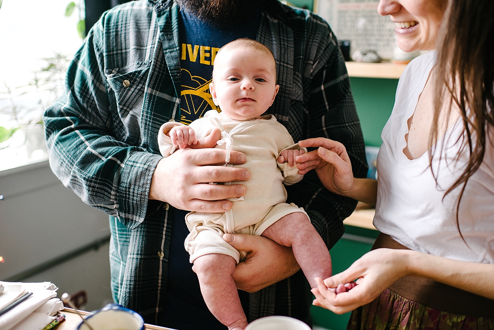 father wearing flannel holding baby daughter while woman holds baby's hand