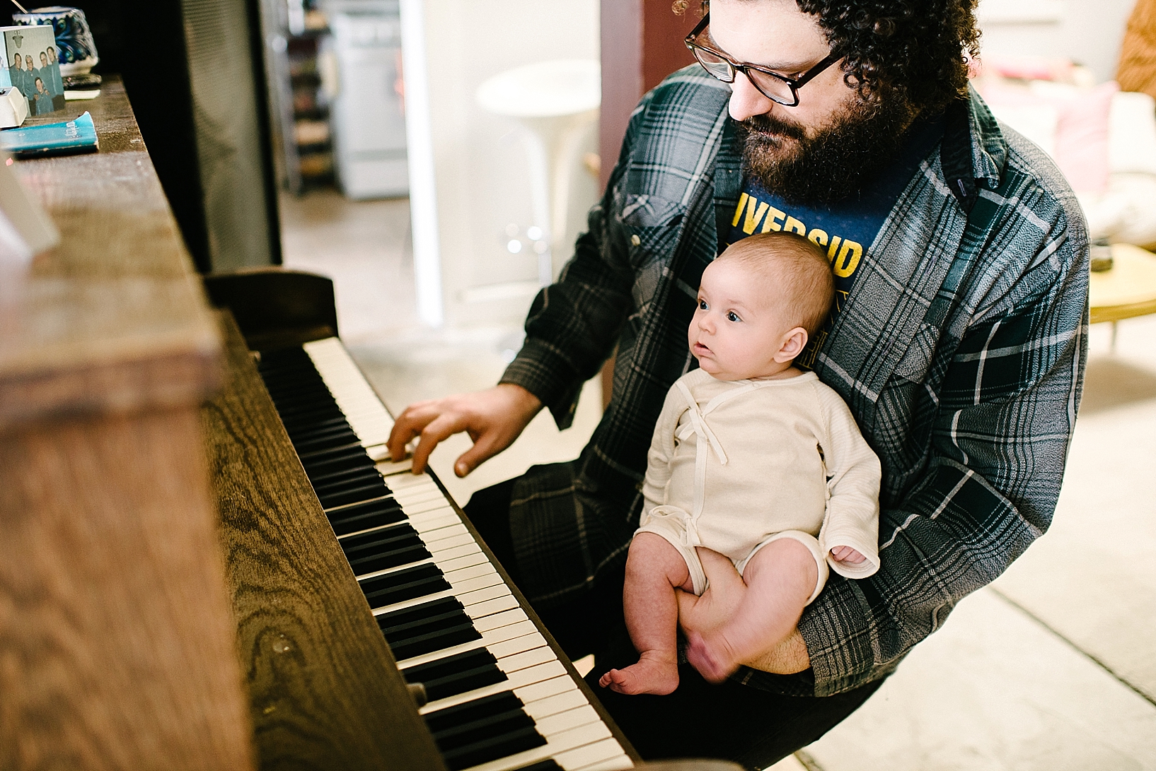 Sam Goodwill playing piano holding infant daughter