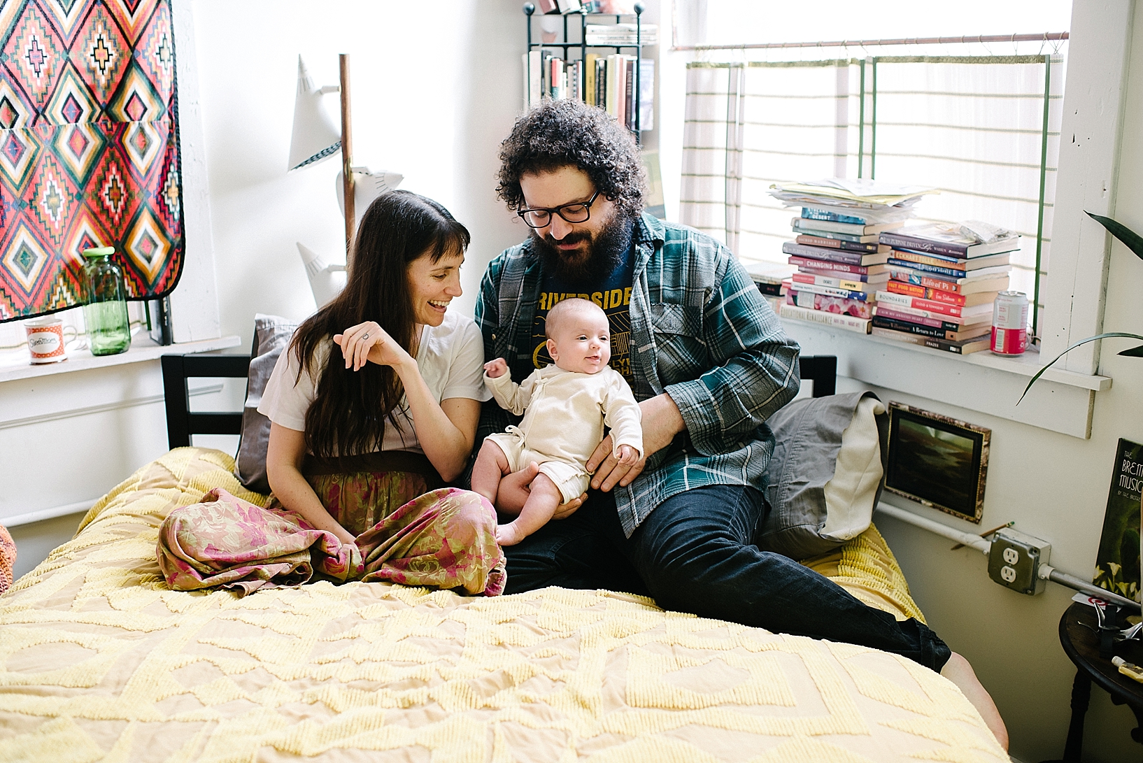bohemian parents sitting on yellow chenille bed with baby daughter