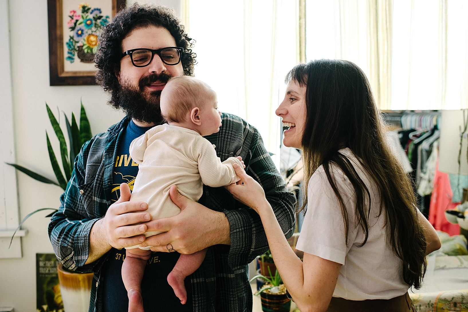 man with curly hair and beard holding baby standing in bedroom with wife