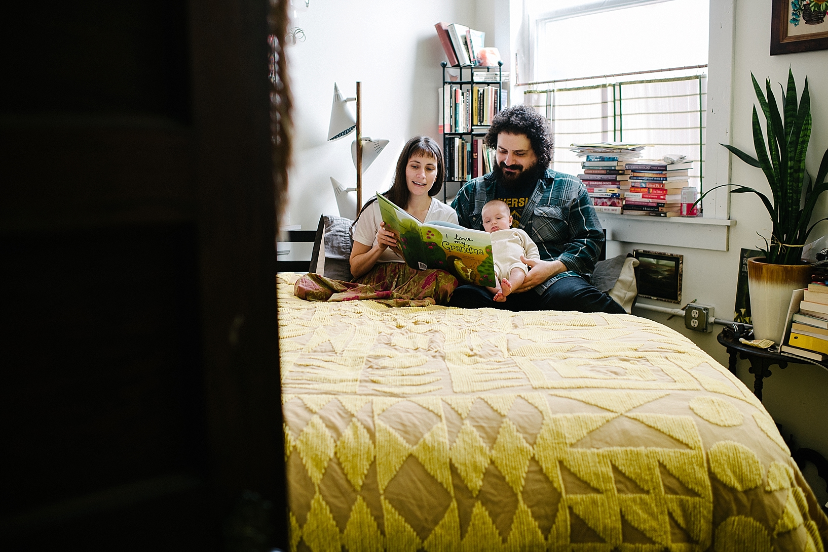 bohemian parents reading book to baby daughter in their lap sitting on bed