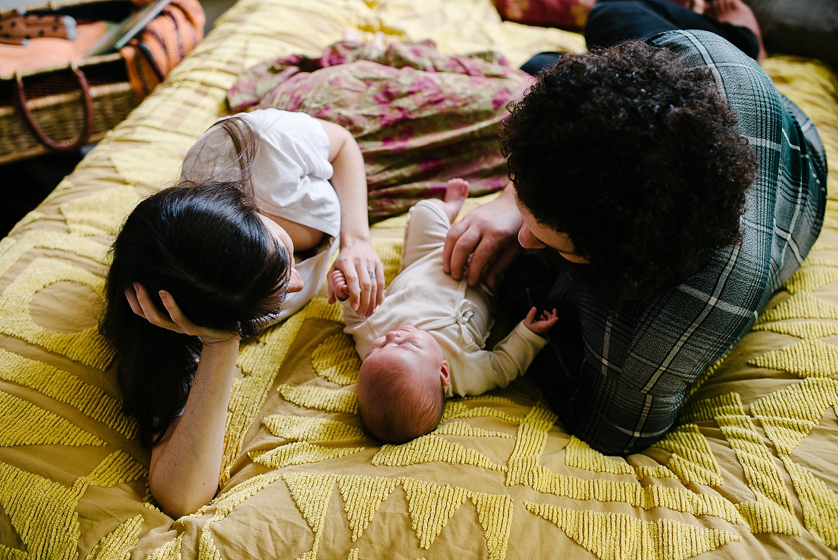 man and woman laying on yellow chenille bedspread with baby daughter in between them