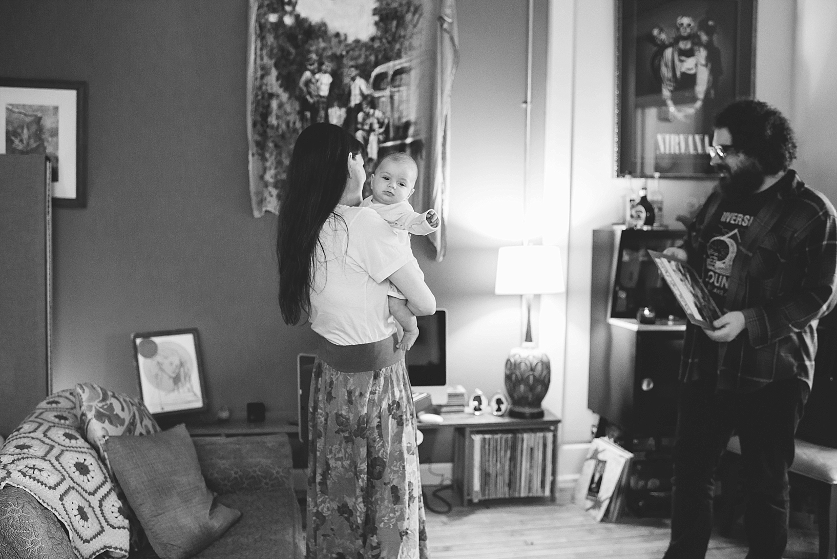 woman holding baby standing in living room while husband puts album on record player