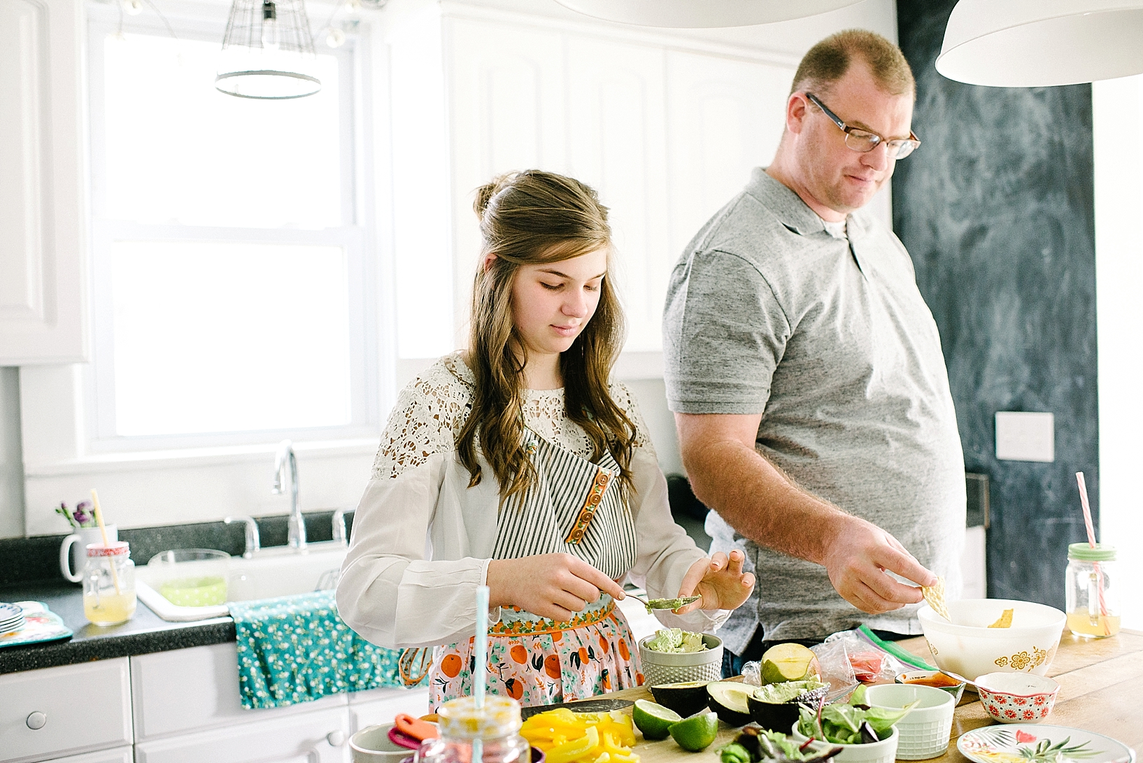 teen girl standing at kitchen island making guacamole with dad standing next to her