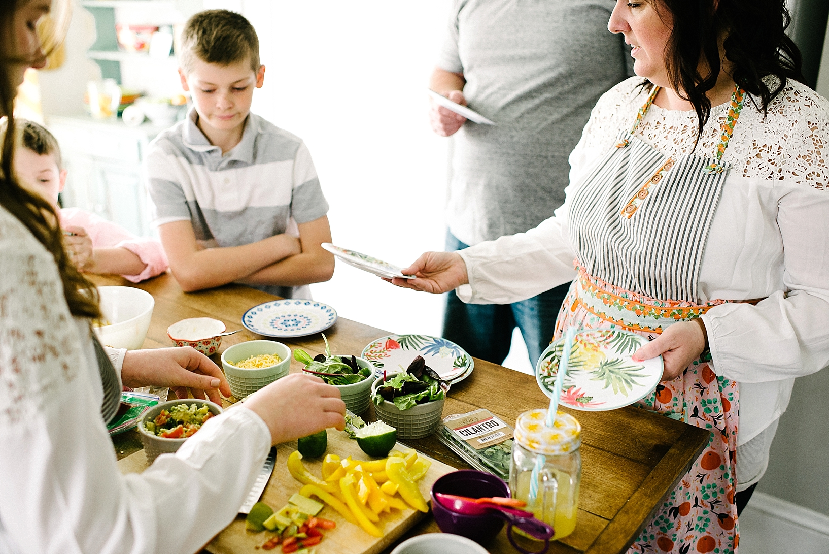 woman wearing patterned apron handing out plates to family members for dinner