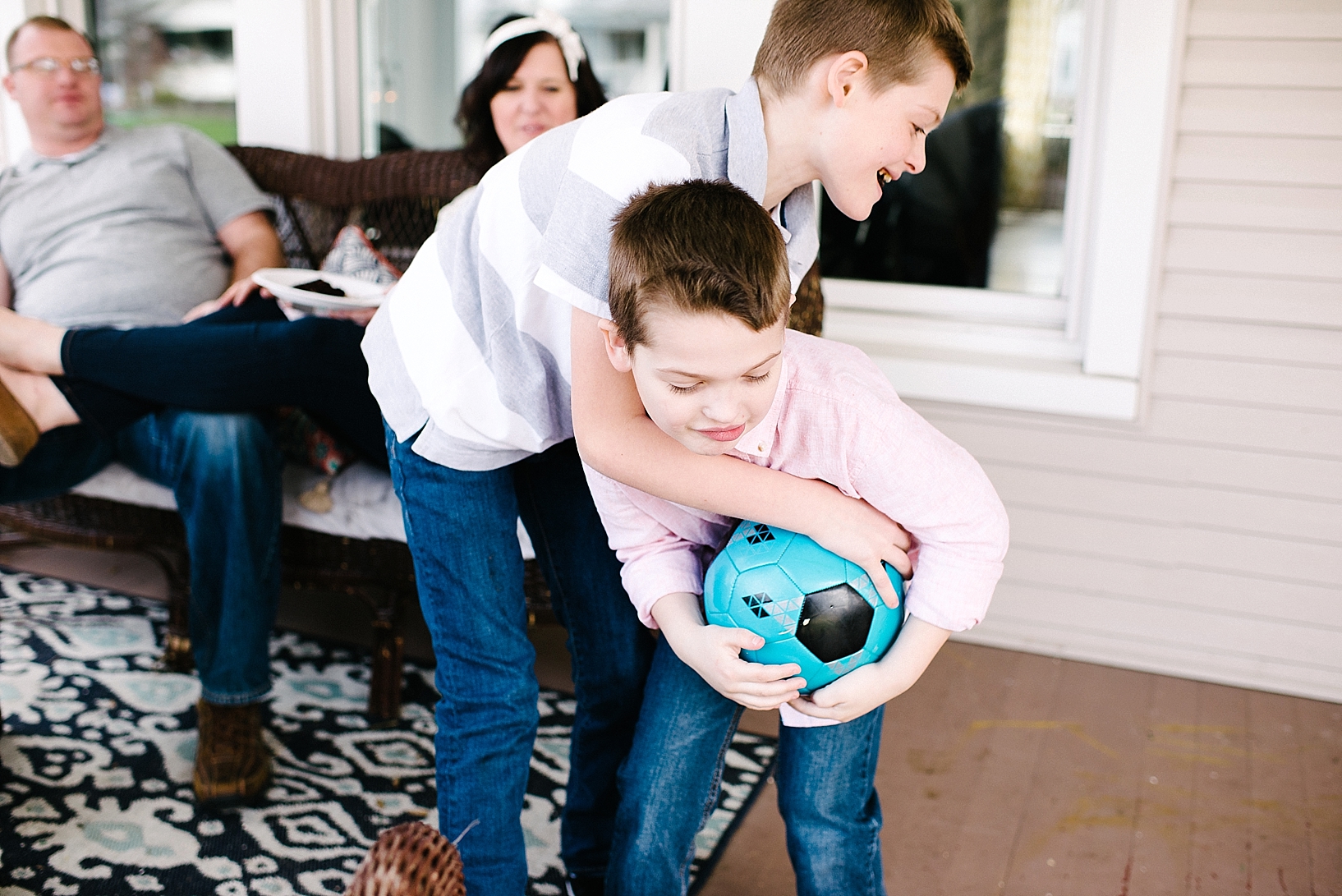 brothers wrestling on front porch over teal soccer ball
