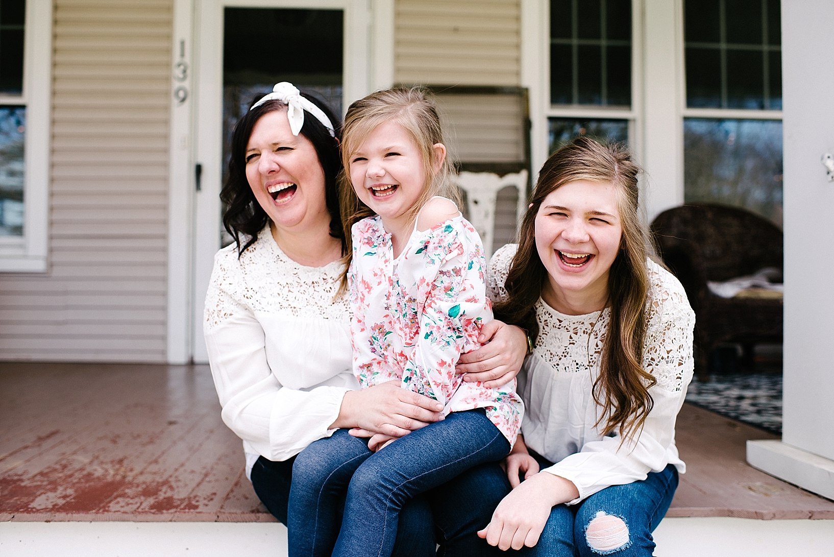 mom sitting on front porch of home with two daughters on spring day