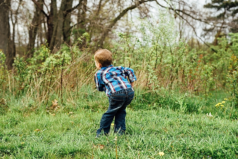 young boy wearing blue and red plaid shirt standing in field of grass shaking his booty