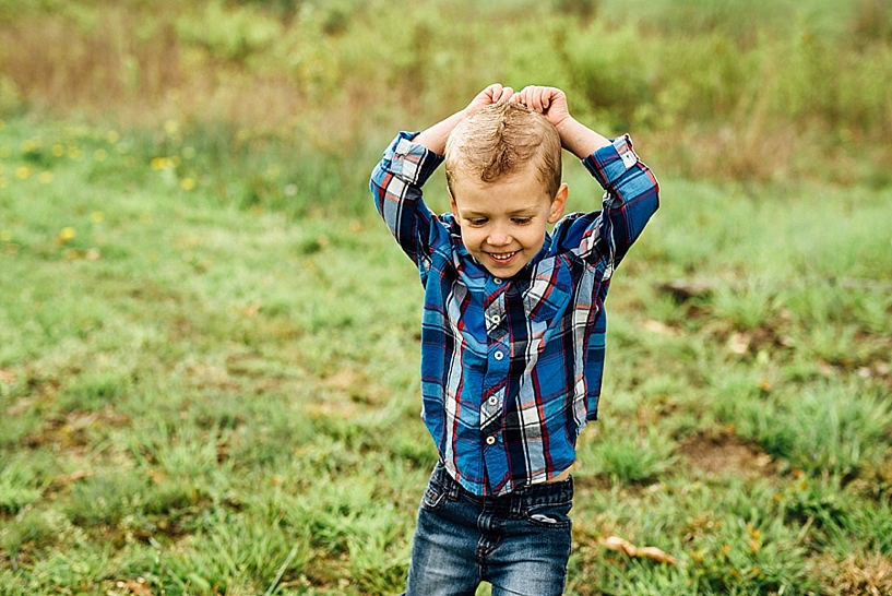 young boy wearing blue converse and blue and red plaid shirt sitting in grass 