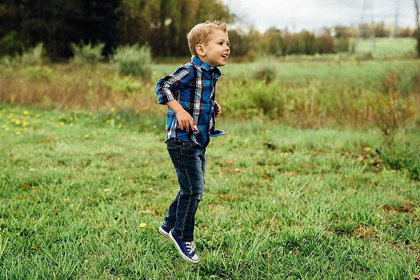 young boy wearing blue converse and blue and red plaid shirt jumping in field