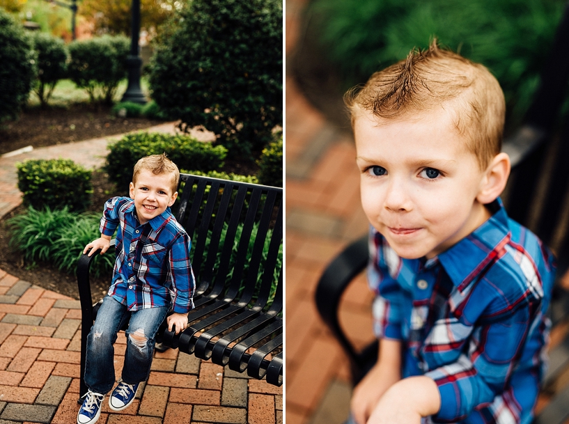 young boy wearing blue converse and blue and red plaid shirt sitting on park bench