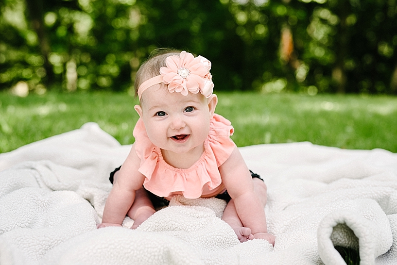 6 month old girl sitting on blanket wearing coral tank top and flower headband