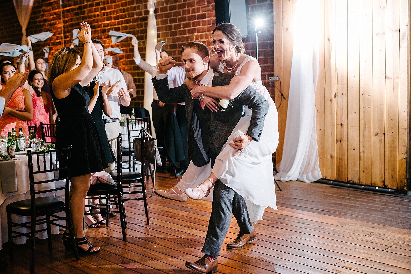 groom carrying bride piggy back into reception hall