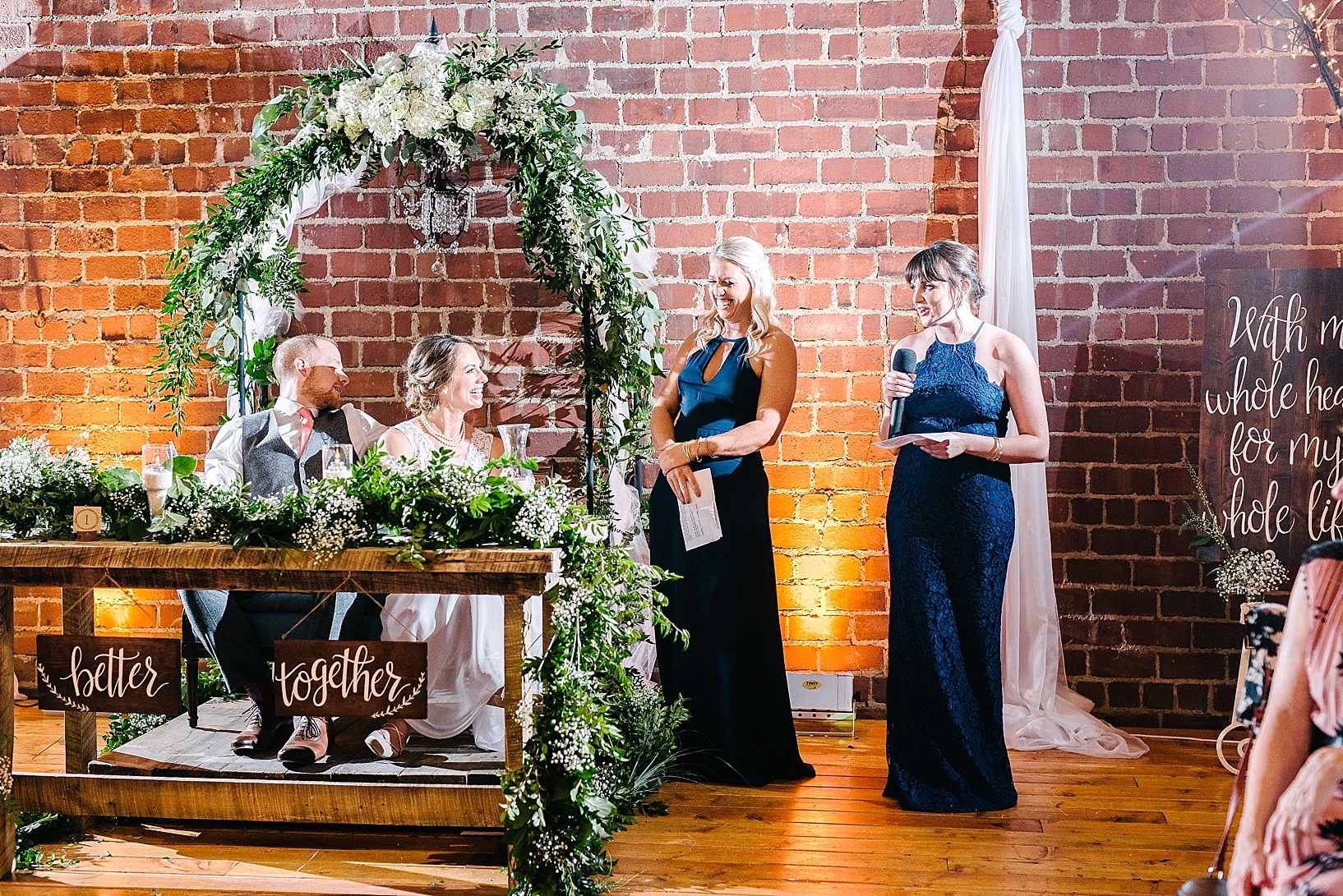 bridesmaids giving toast to bride and groom standing against brick wall