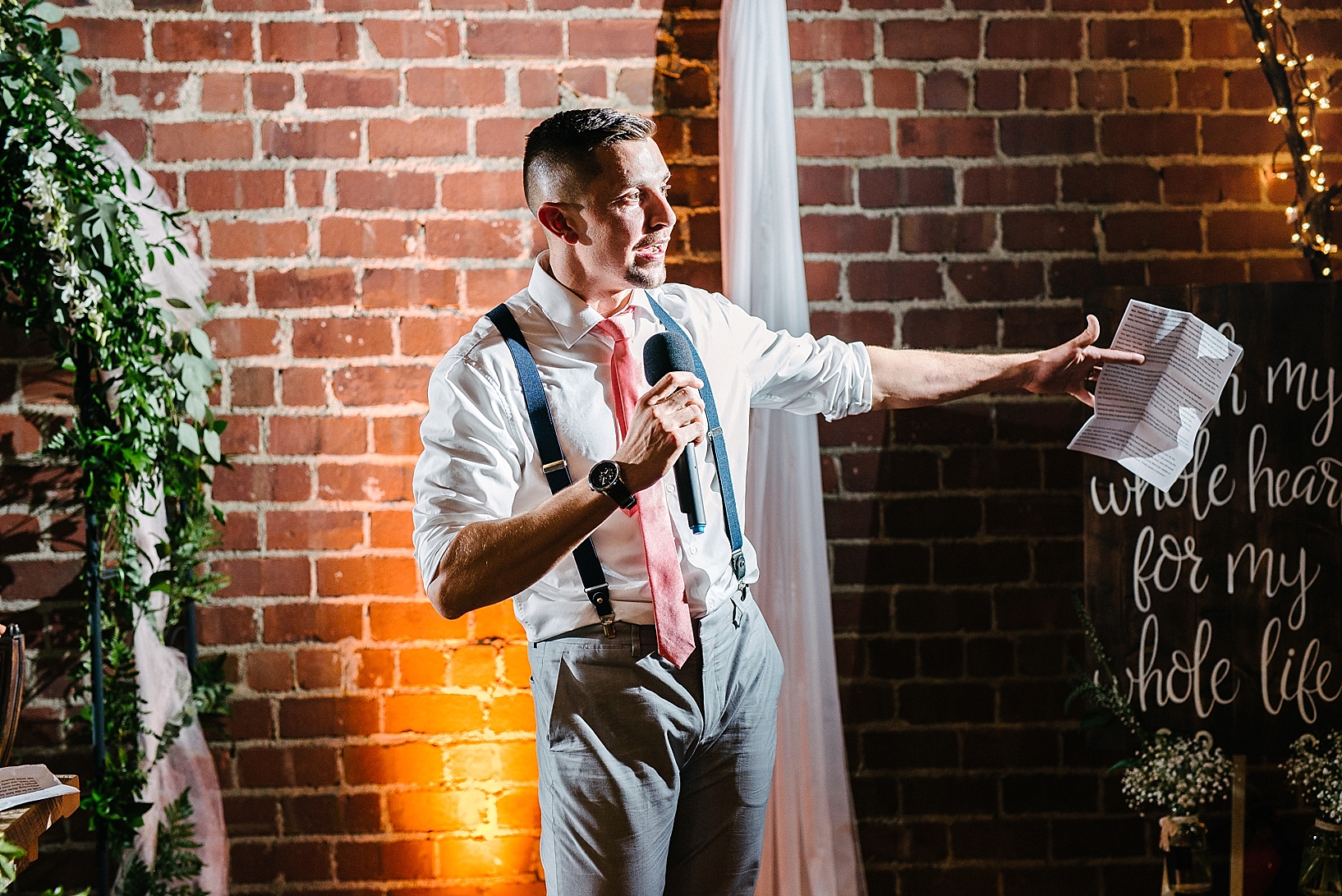 groomsman giving toast to bride and groom standing against brick wall