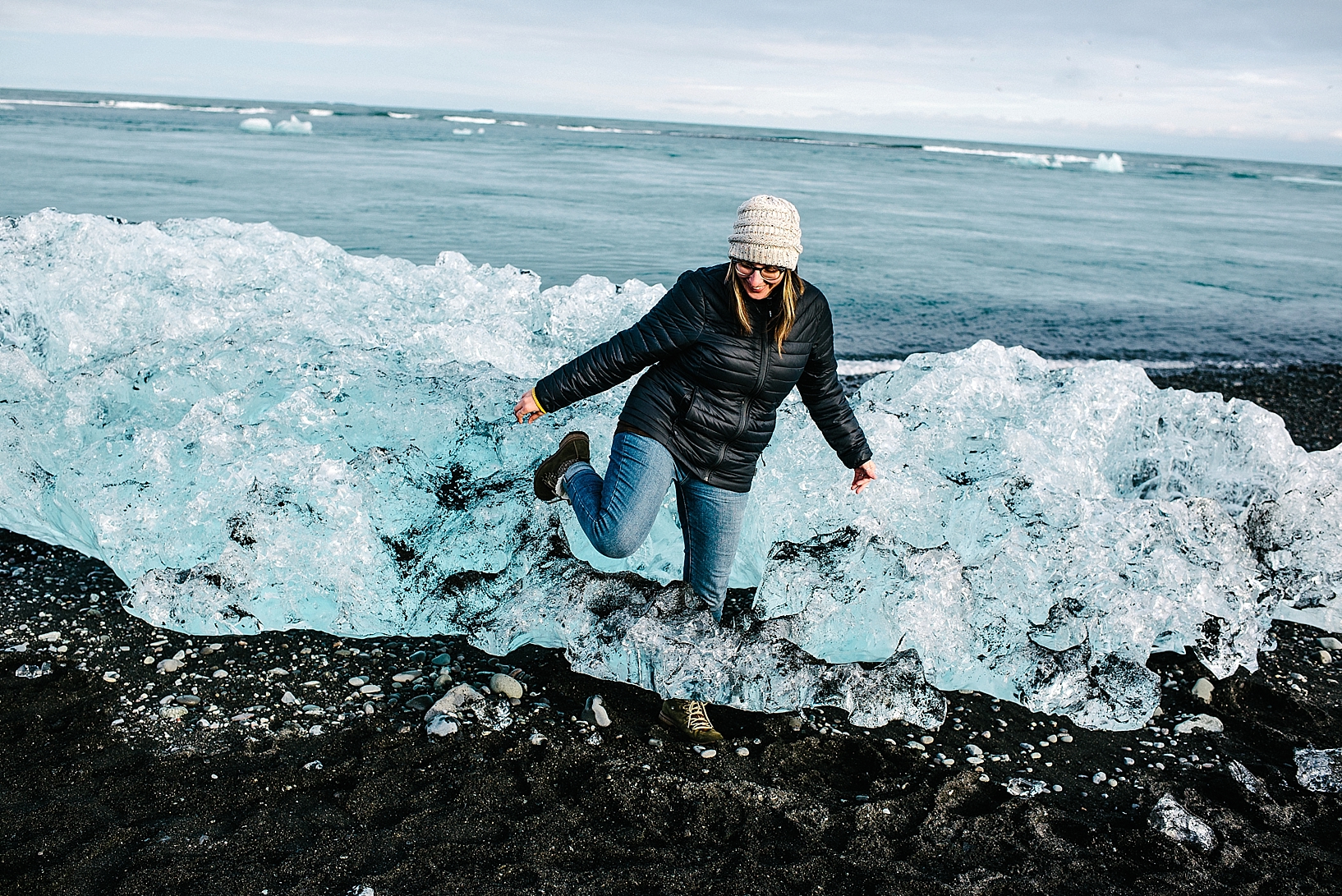 woman climbing through iceberg on black sand beach at Jokulsarlon Iceland