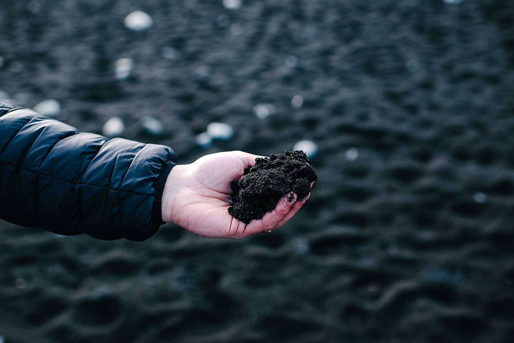 man holding handful of black sand Jokulsarlon Iceland