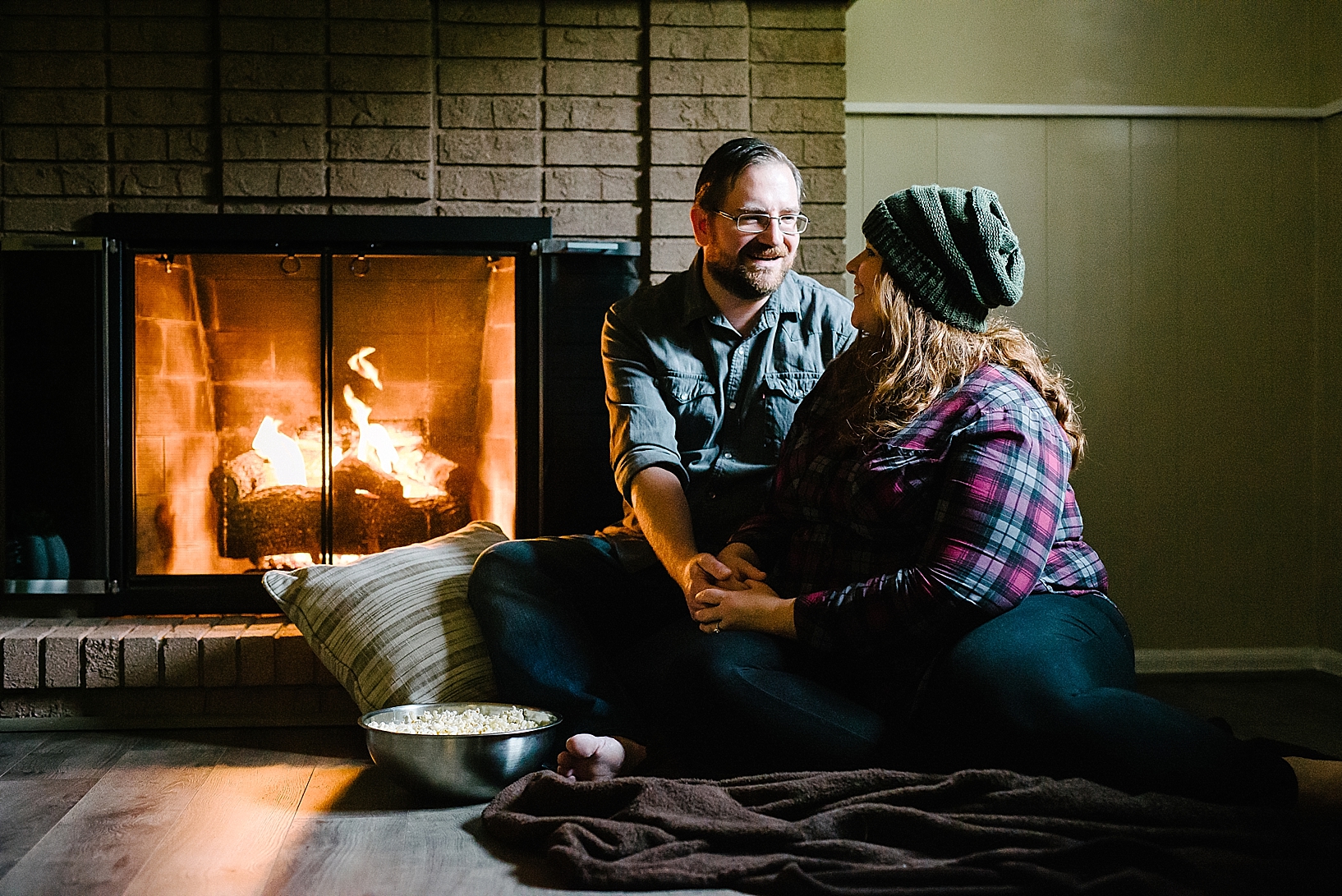 man and woman sitting on floor by fireplace with bowl of popcorn