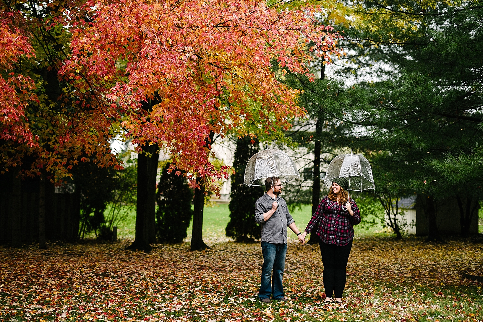 couple standing under clear umbrellas holding hands under trees