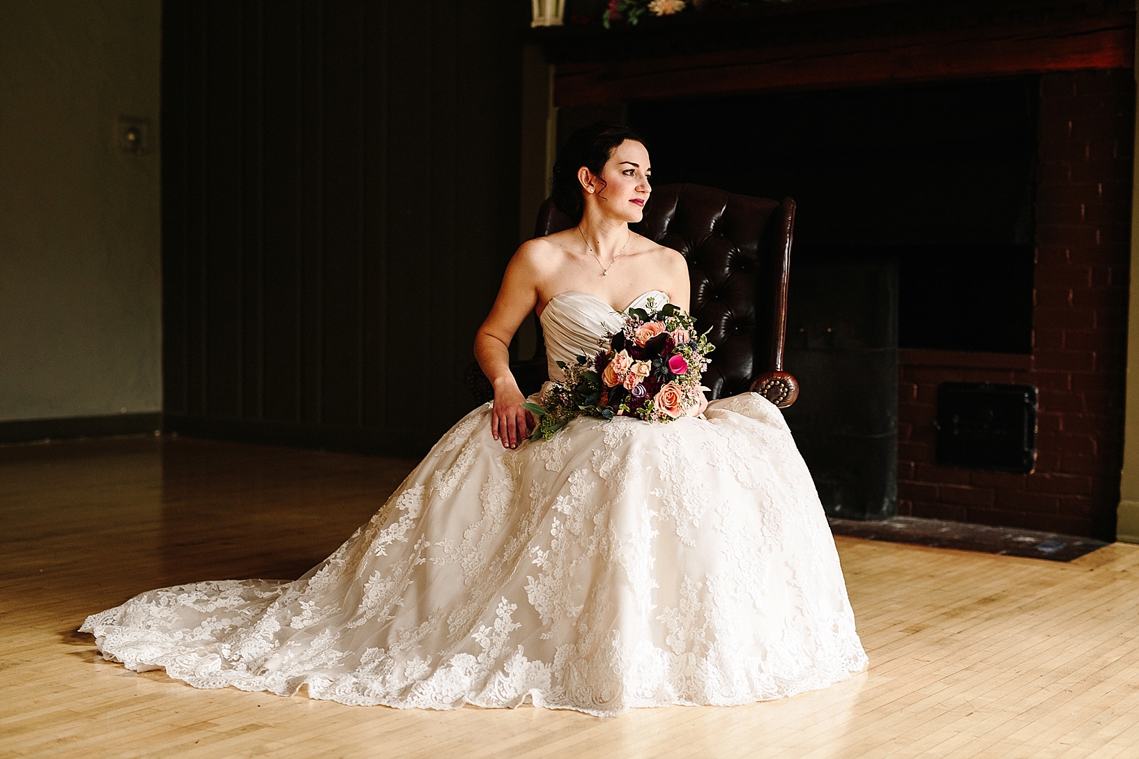 bride sitting in leather arm chair in front of fireplace