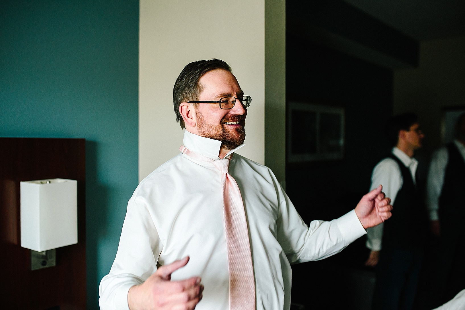 groom wearing pink tie getting ready in hotel room