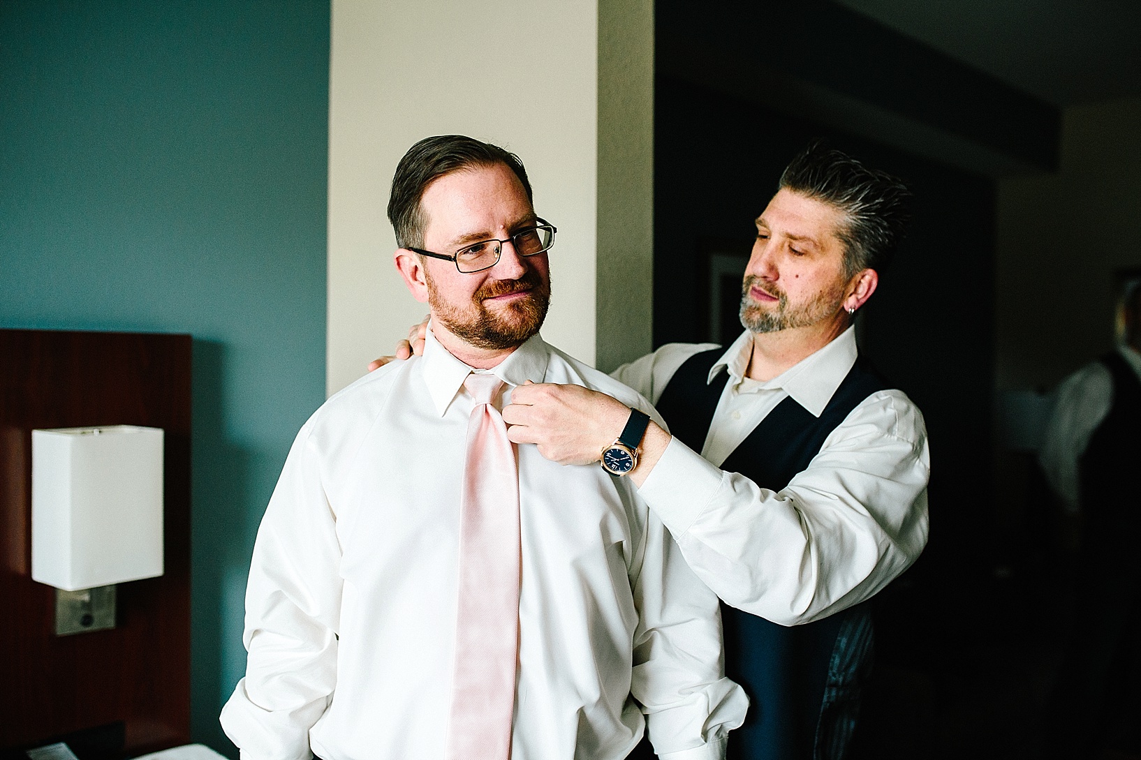 groomsmen helping groom get dressed in hotel room