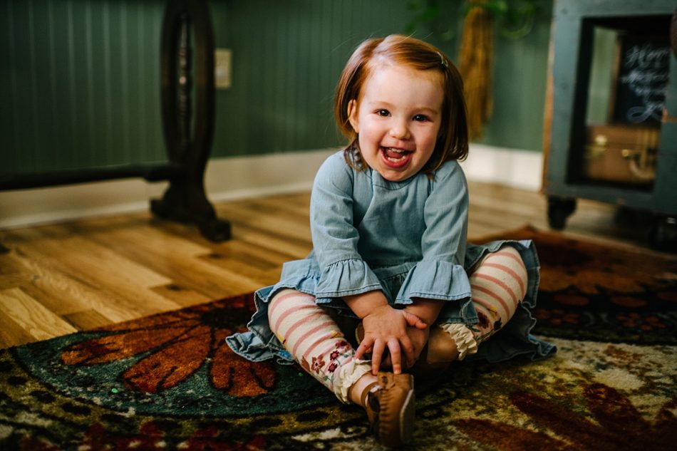 little girl in denim dress sitting on colorful area rug