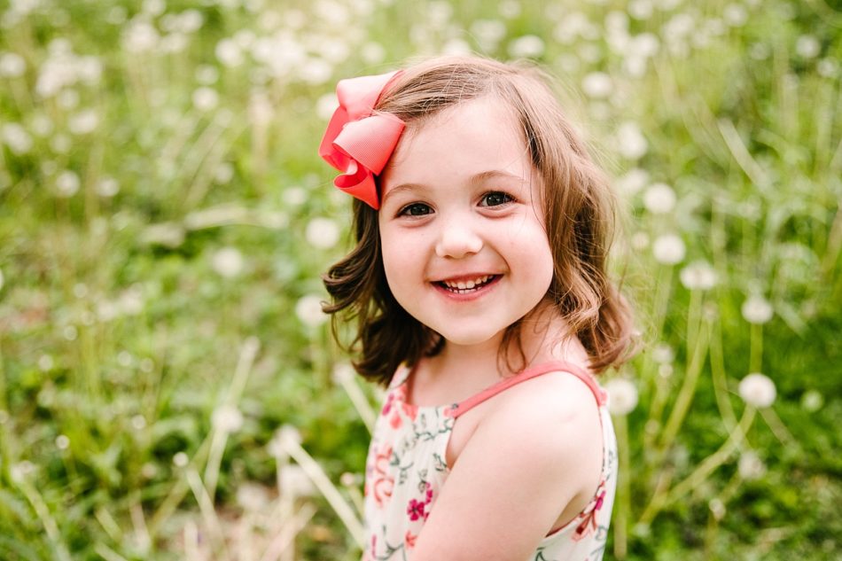 Young girl smiles at the camera with a big red bow in her hair and a sundress in a field