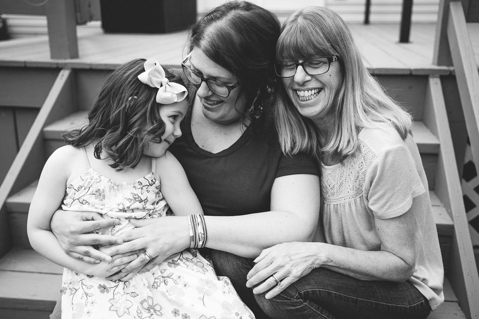 Grandma, mom, and daughter smile on backporch steps during generational family session