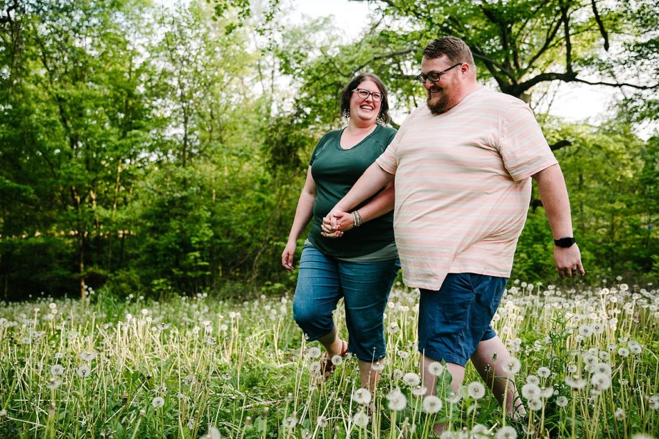 A couple holds hands and walks through field of flowers smiling