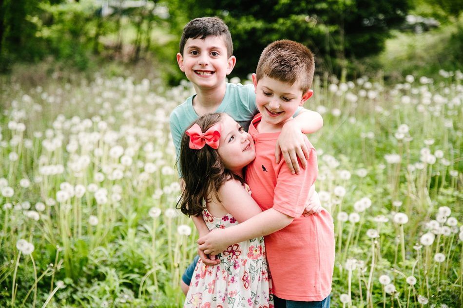 Three siblings hug in a field of flowers in backyard generation family session