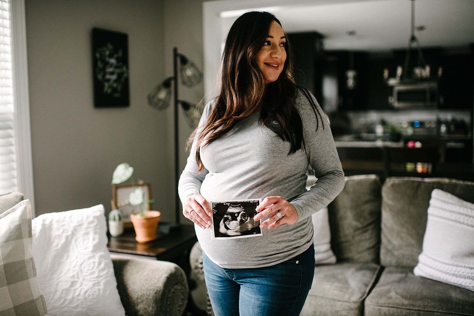 Pregnant woman holds sonogram to belly neutral nursery maternity shoot
