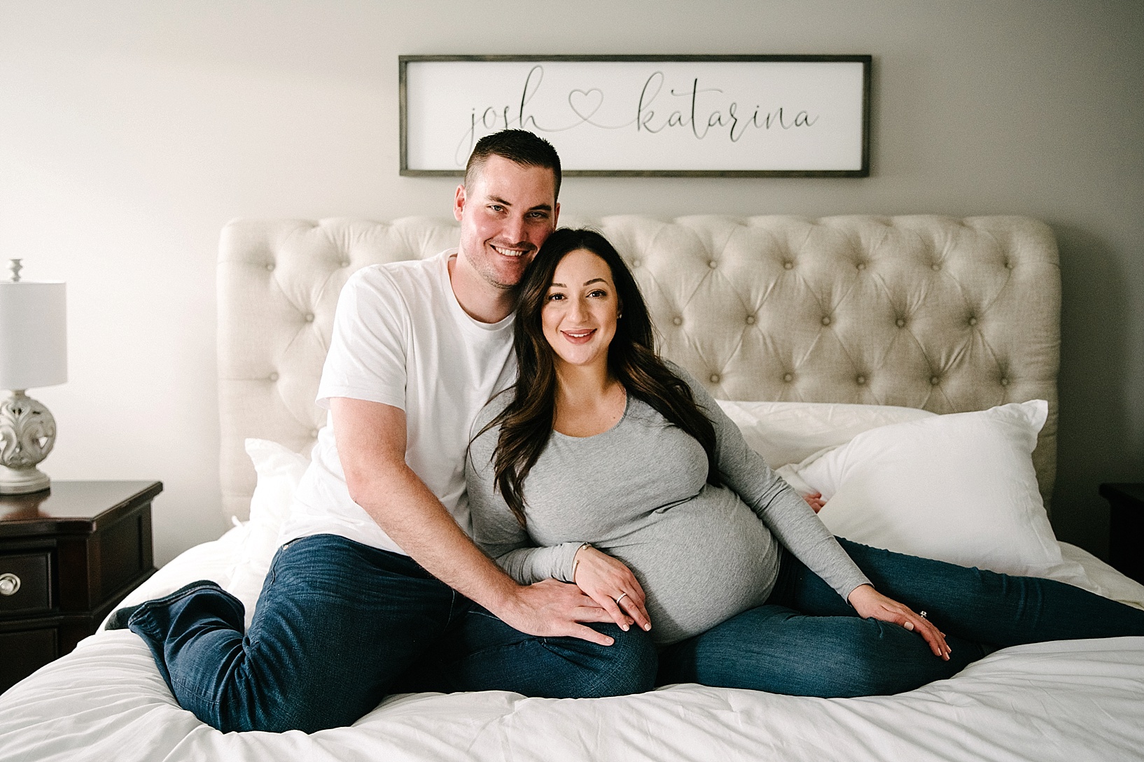 Husband and pregnant wife smile while sitting on bed