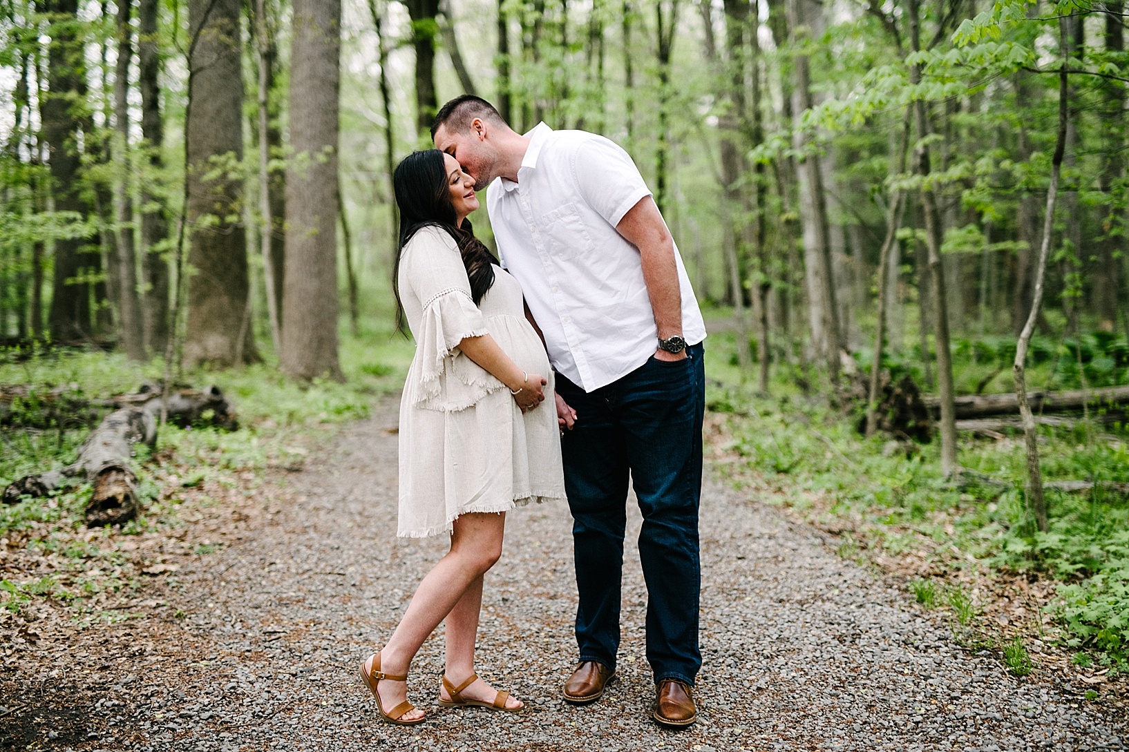 Man kisses pregnant wife's cheek in woods maternity photography session