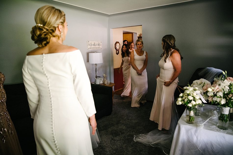 Bridesmaids come in after bride puts on wedding gown